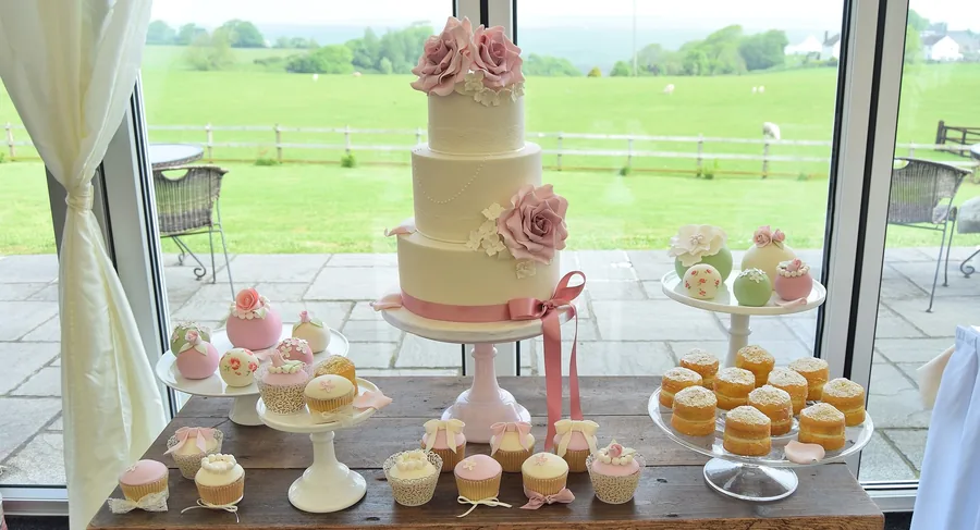 A tiered wedding cake and matching cupcake display set up by a window at a Piece of Cake Wales wedding